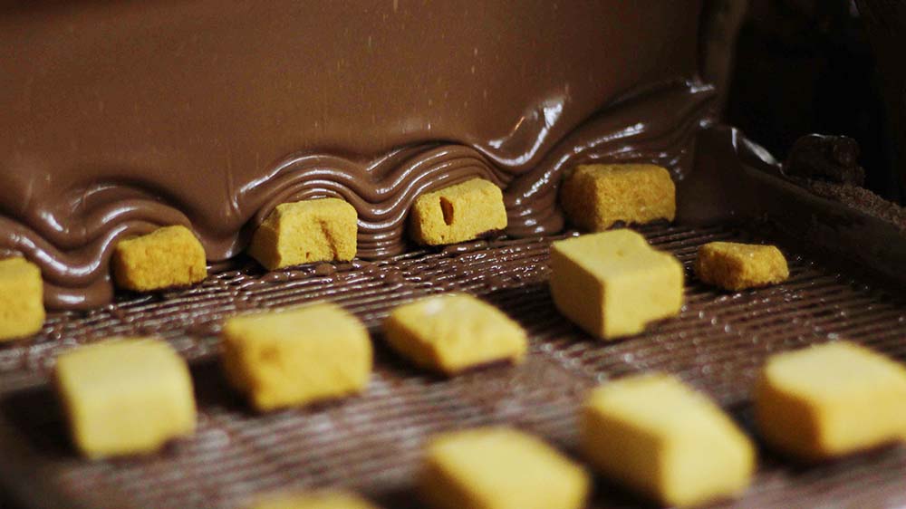 Sponge candy being coated in chocolate