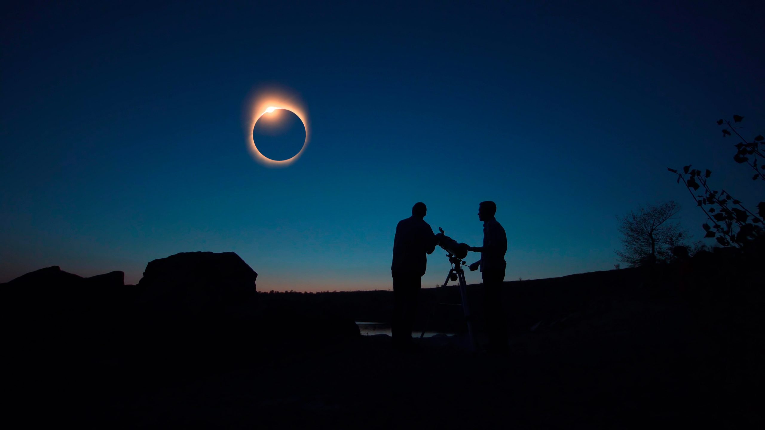 Black silhouettes of people looking through telescope on sun eclipse on shore.